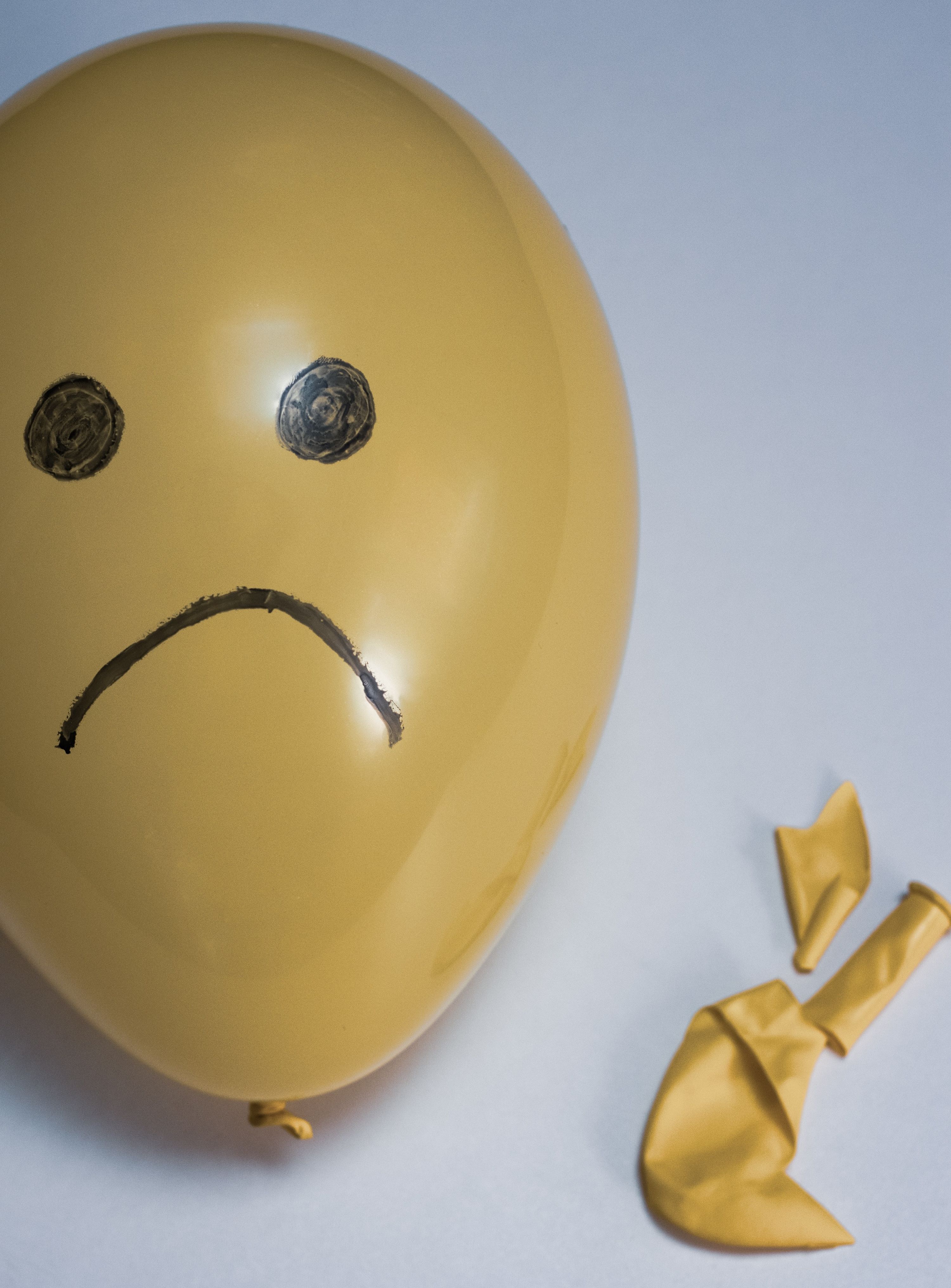 Yellow balloon with a frowny face drawn in black marker. A broken balloon lies next to it