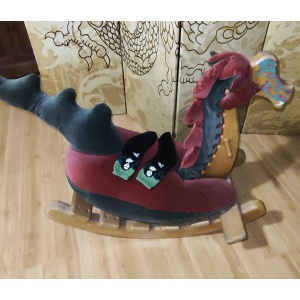 Red and green rocking dragon sitting in front of a yellow screen with a chinese dragon drawn on it. A pair of socks with images of the Mona Lisa sit on its back